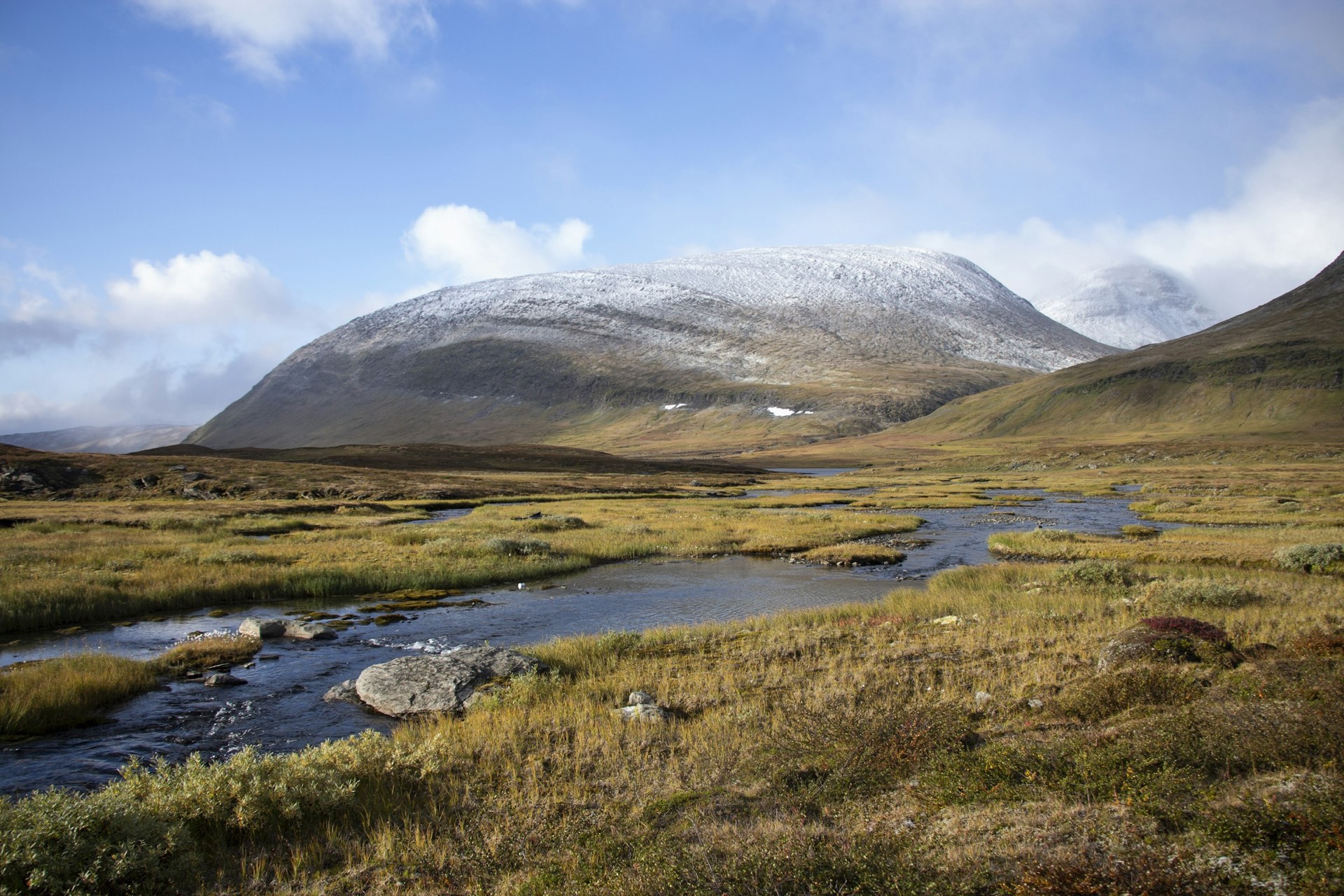 A stream through russet autumn ground at Abisko, snow-capped mountain behind